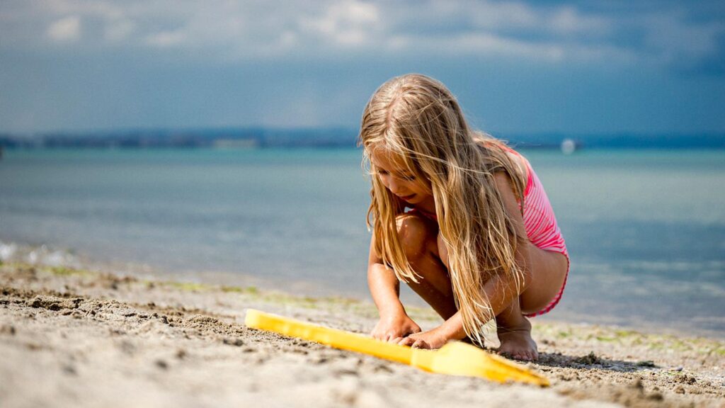 En flicka leker vid stranden i Grekland och bygger med sand.