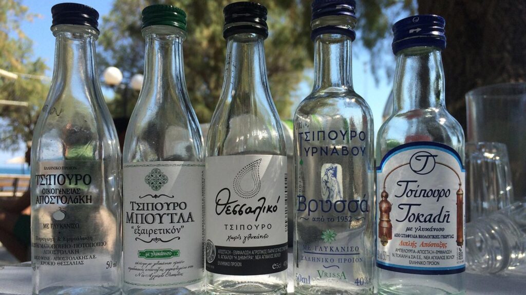 Flera flaskor av grekisk alkohol står framme vid Medelhavet.