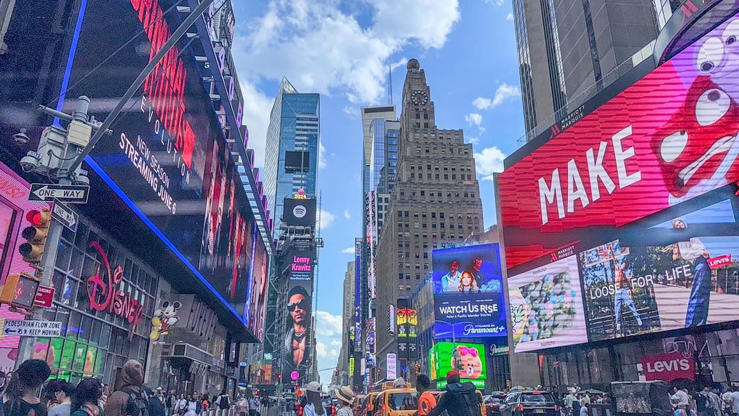 En livlig gata i Manhattan med stora reklamskärmar och människor som handlar.