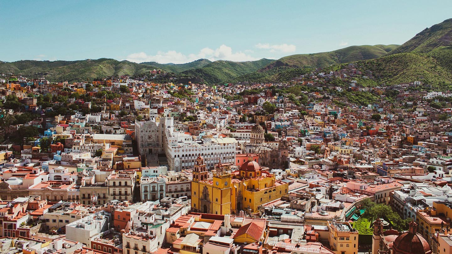 En färgglad vy av Guanajuato med berg i bakgrunden och historiska byggnader.