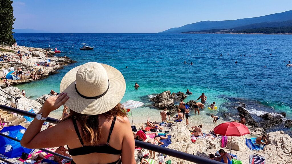 En kvinna i hatt njuter av en solig dag på stranden i Rabac, Kroatien.