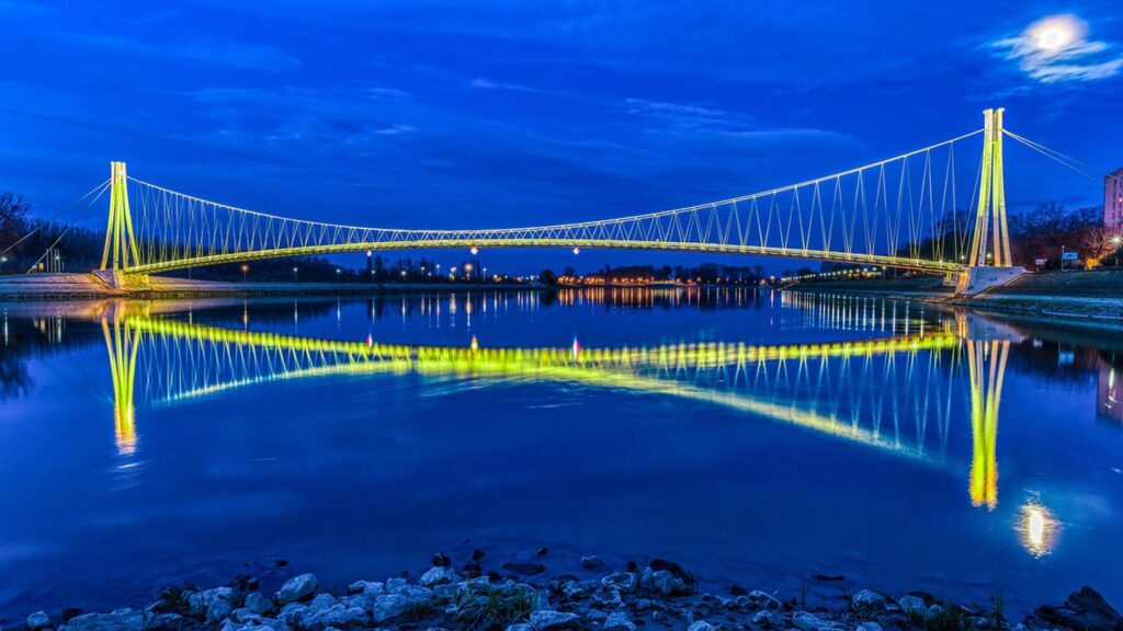 Bilden visar en vacker bro i Osijek, Kroatien, med reflektioner i vattnet.