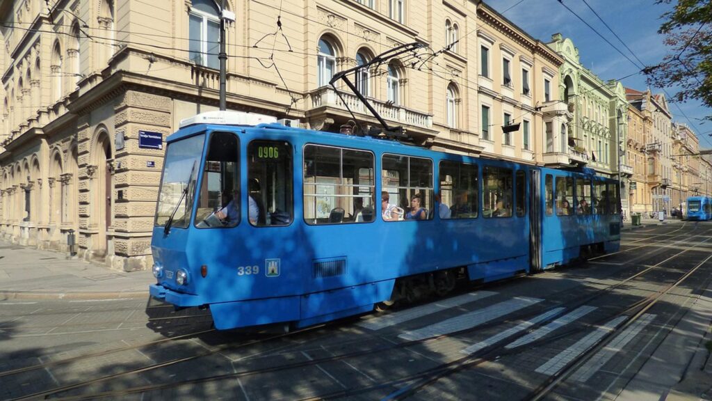 En blå spårvagn kör genom Zagreb, Kroatien, omgiven av klassisk arkitektur.