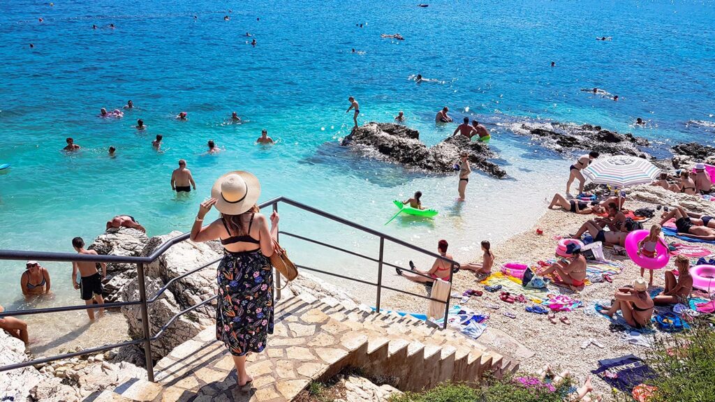 En solig dag på stranden i Rabac, Kroatien, med många badande och solande människor.
