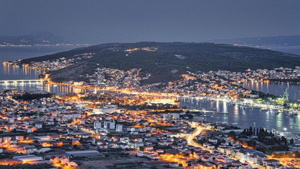 Trogir vid skymning med glittrande ljus och spegelbild i vattnet.