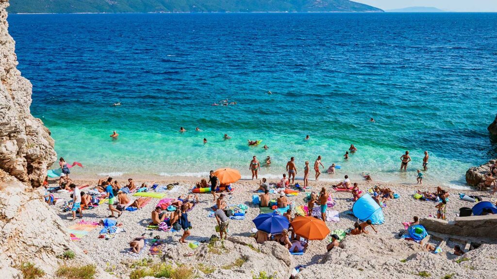 Turister njuter av en solig dag på Brsec stranden i Kroatien.
