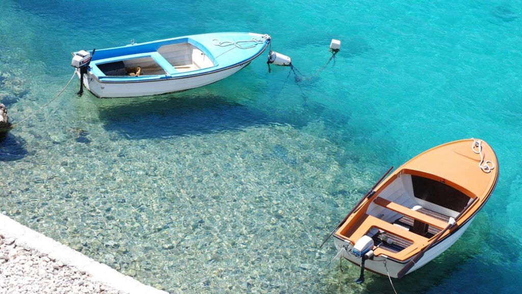 Två båtar ligger stilla på det turkosa vattnet i Adriatiska havet, Kroatien.