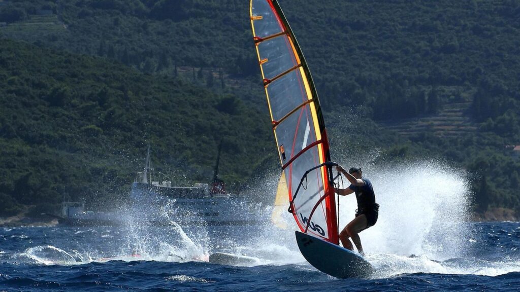 En vindsurfare rider på vågorna i Pelješac, Kroatien, med frodig grönska i bakgrunden.