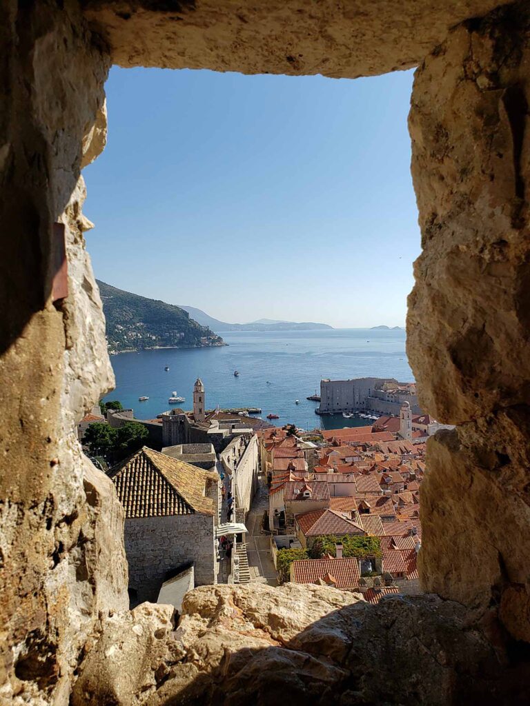 Utsikt över Dubrovnik och Adriatiska havet med tak och murar i förgrunden.