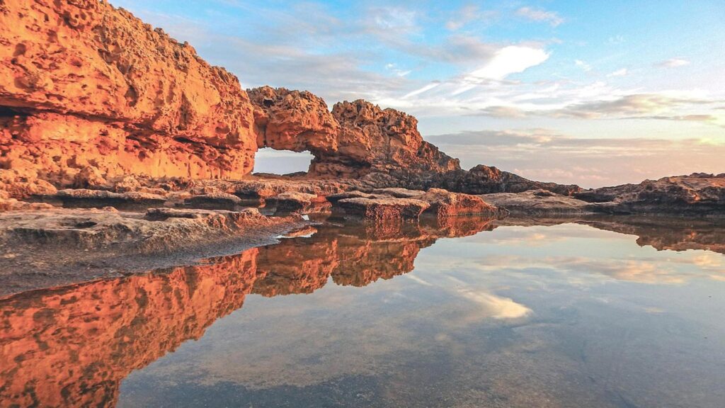 Sandstensbergformationer i Ayia Napa, Cypern, speglas i stilla vatten.