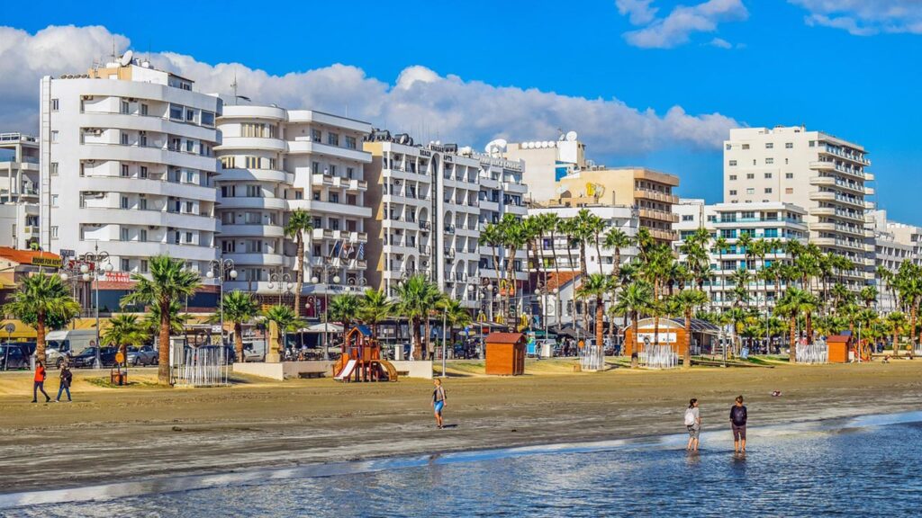 Finikoudesstranden i Larnaca, Cypern, med palmträd och moderna byggnader.
