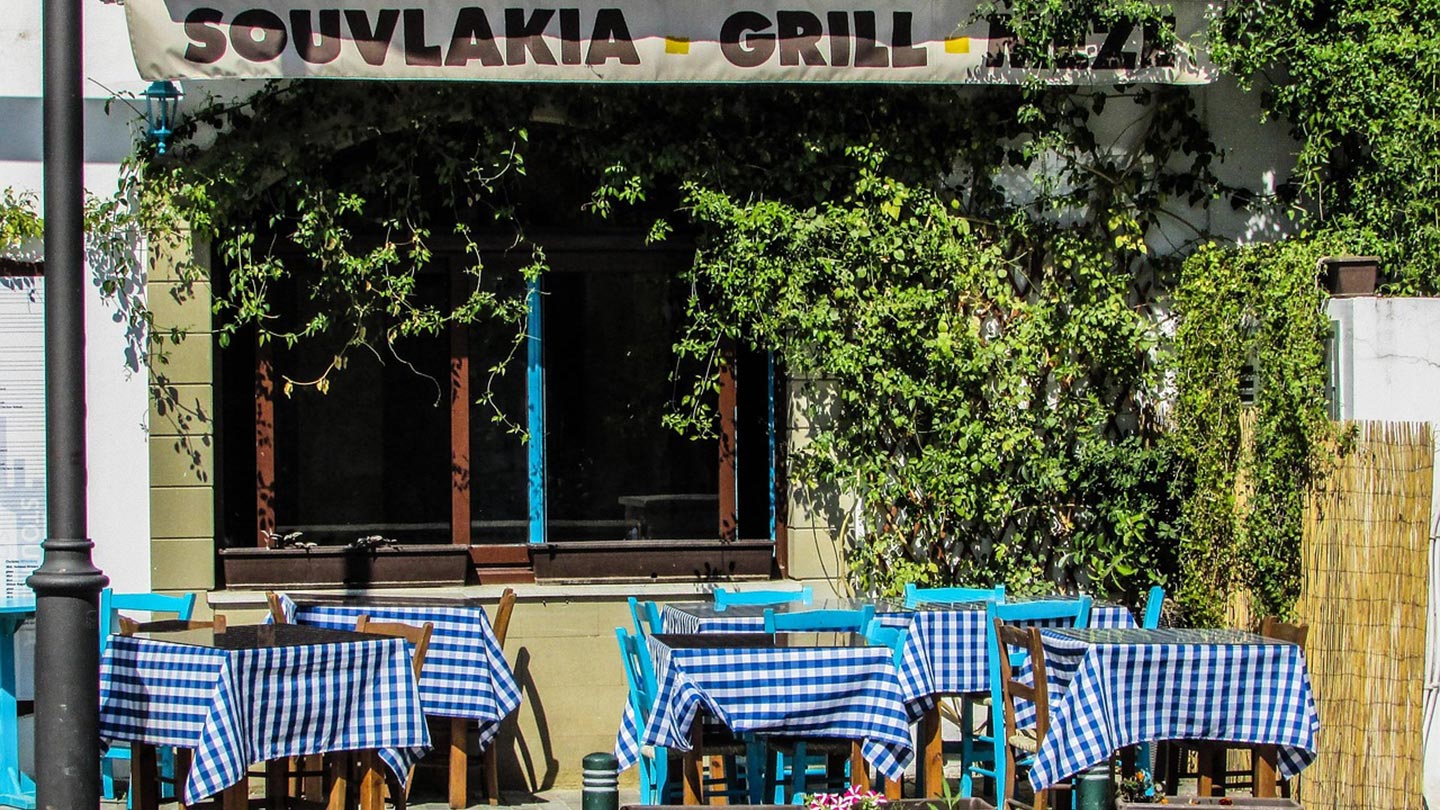 En krog i Larnaca, Cypern, med blå rutiga dukar och grönskande omgivning.