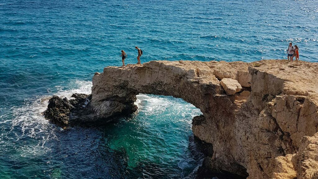 Människor promenerar på en klippbåge vid kusten i Ayia Napa, Cypern.