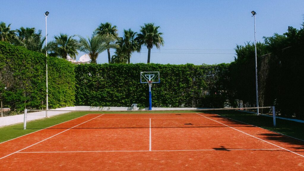 En tennisbana med basketkorg i Larnaca, Cypern, omgiven av palmer och grönska.