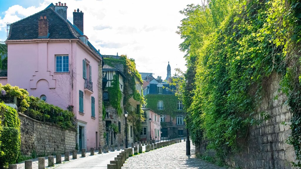Rosa hus omgivna av grönska i Montmartre, Paris, med kullerstensgata.