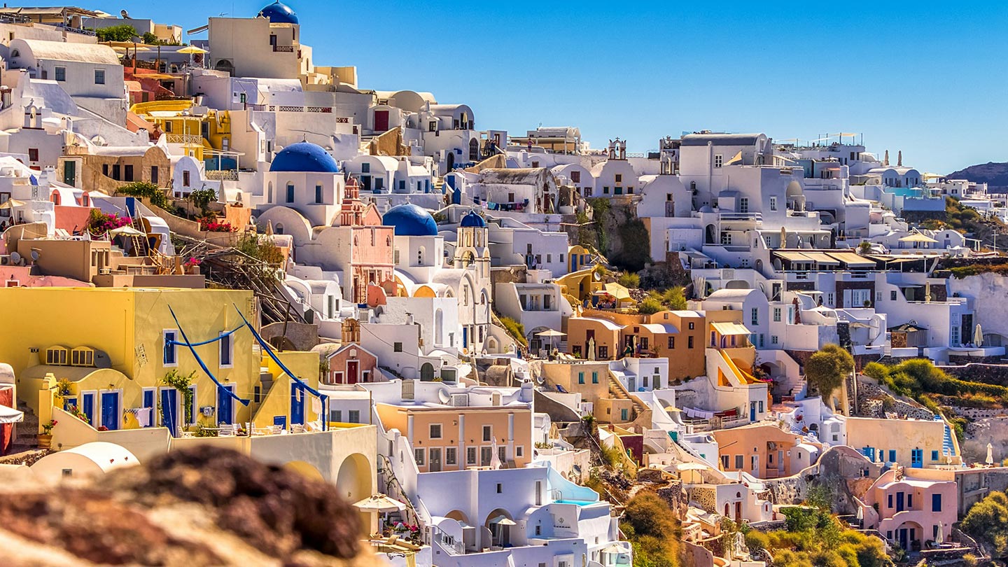 En färgglad vy av hus i Santorini, Grekland, med blå kupoler och soligt väder.