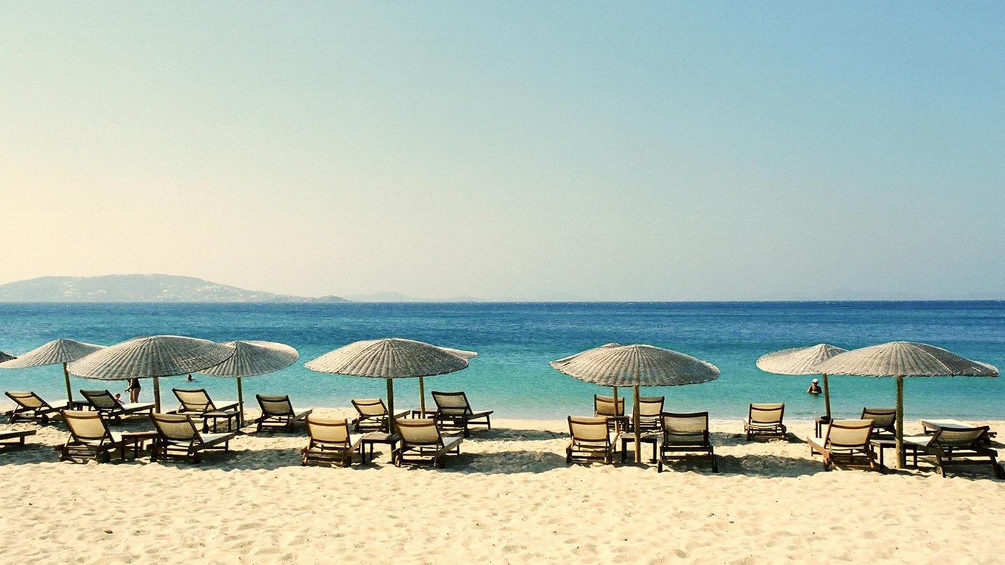 En solig strand i Santorini, Grekland, med solstolar och parasoll.