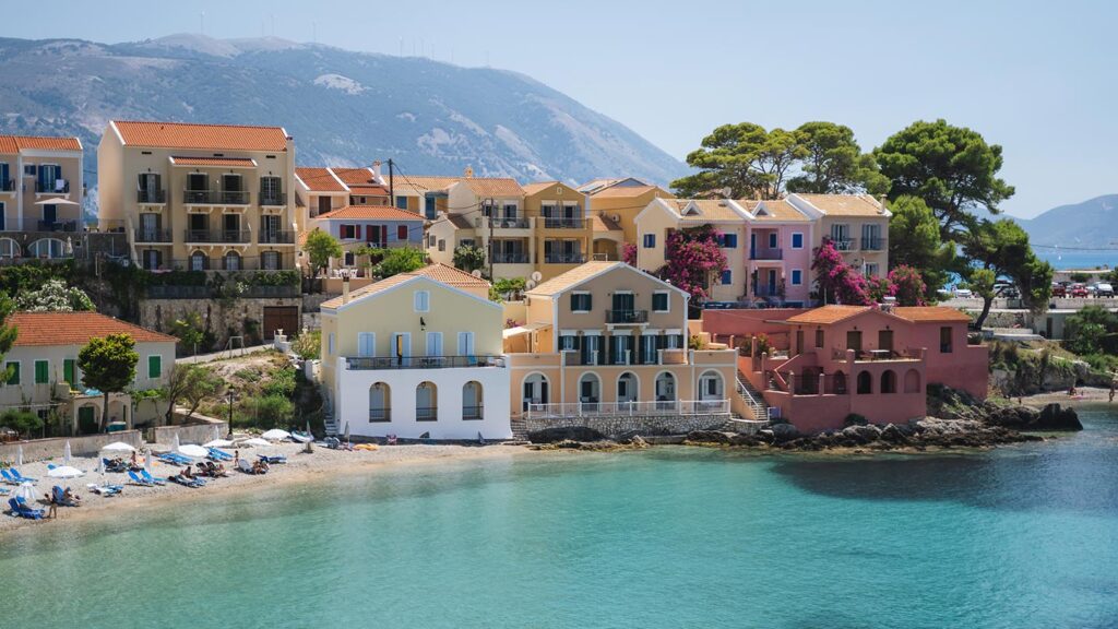 Bild av Assos i Kefalonia, Grekland, med färgglada hus vid en lugn strand.