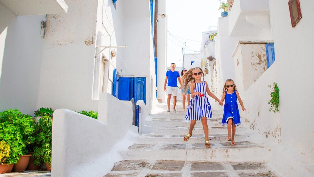 En glad barnfamilj promenerar neråt på gatan i Mykonos, Grekland.