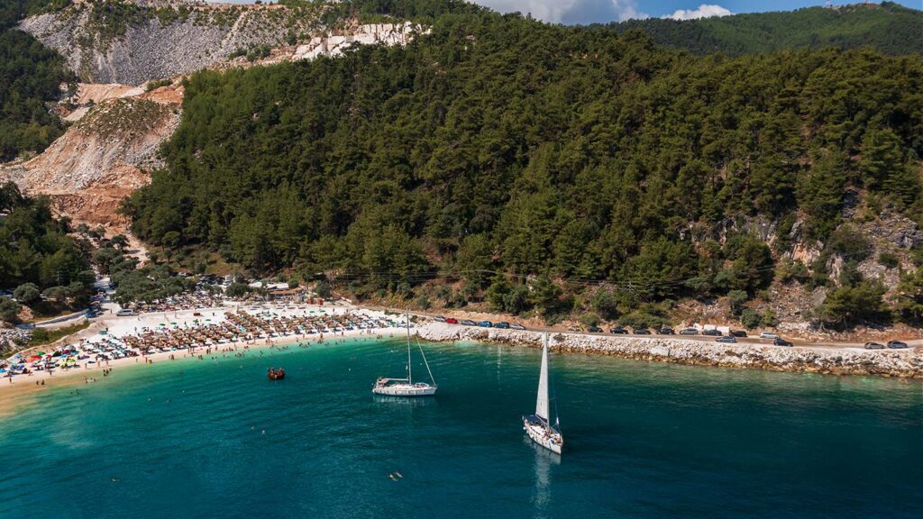 Marmorstranden på Thassos i Grekland med segelbåtar och solande gäster.