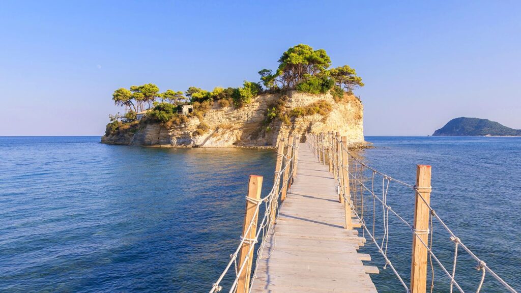 En träbro leder till Cameo Island vid Zakynthos i Grekland. Klart vatten och blå himmel.