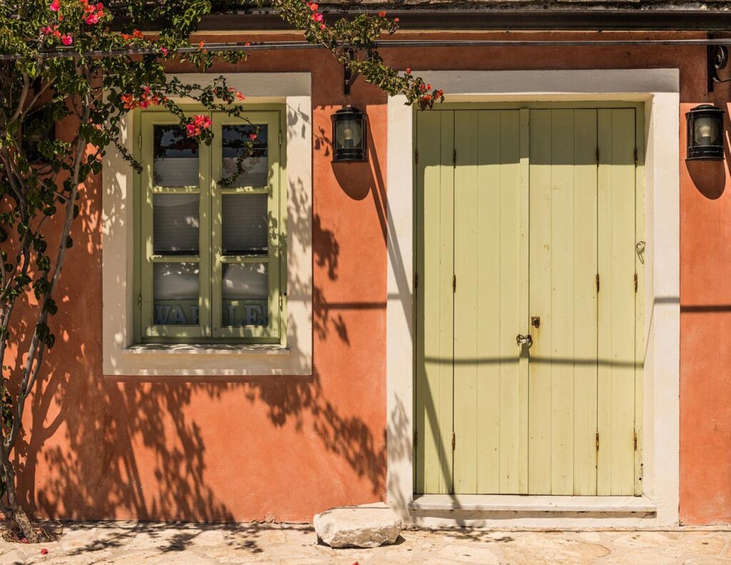 En grön dörr på en vägg i Fiskardo, Kefalonia, med blommor och skuggor.
