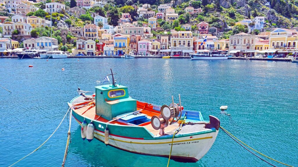 En färgglad fiskebåt vid Symi, Grekland, med pittoreska hus i bakgrunden.