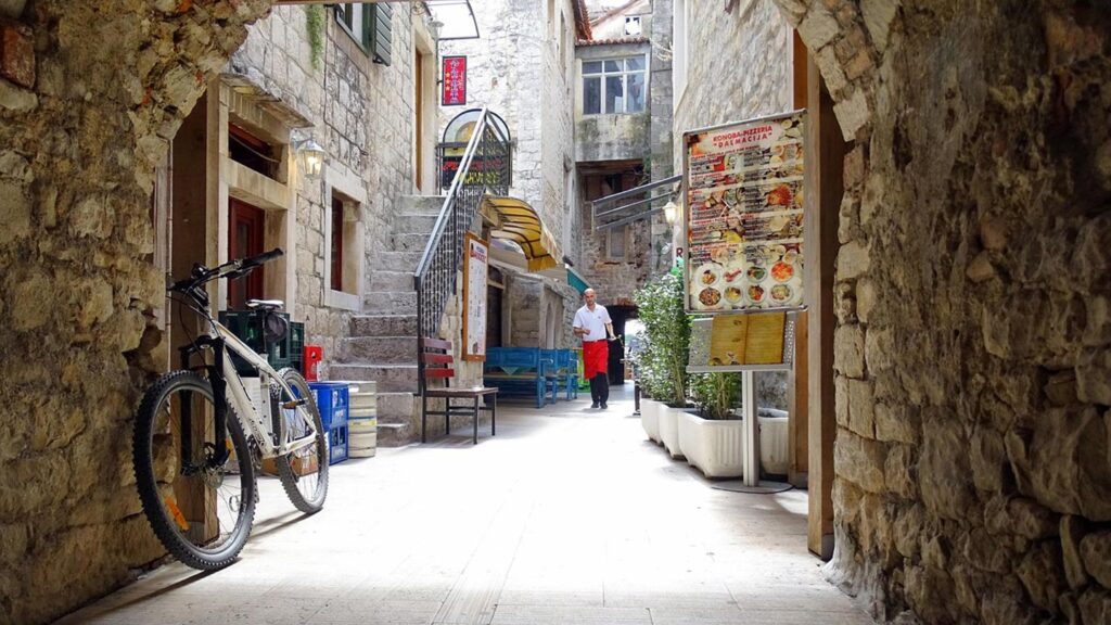 En mysig gränd i Trogir, Kroatien, med restauranger och en cykel.