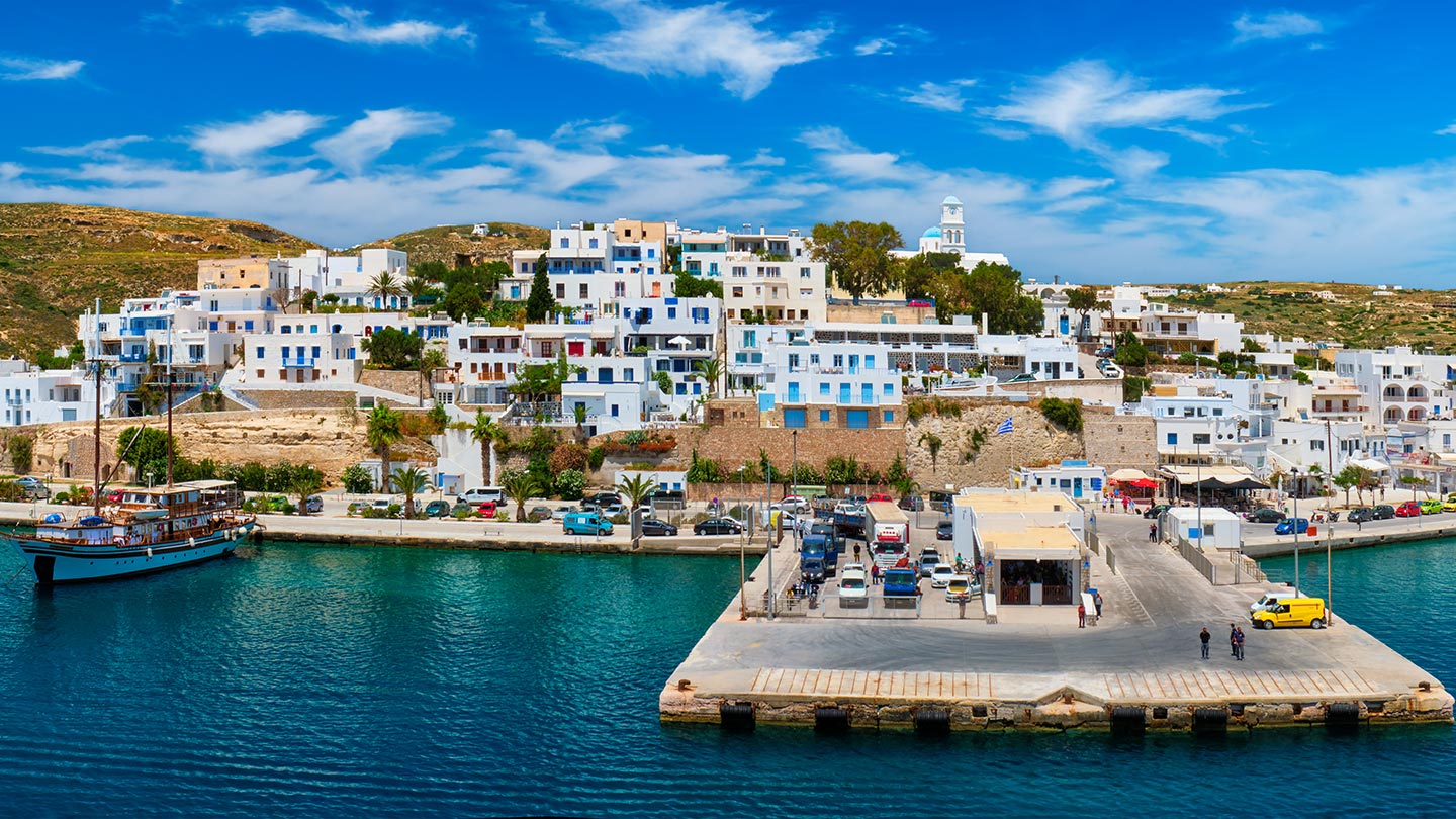 En vacker hamn i Adamas, Milos, Grekland med vita hus och klarblått hav.