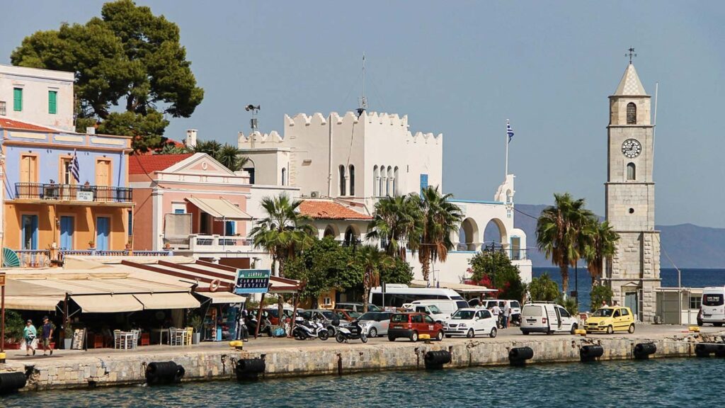 Klocktornet vid hamnen i Gialos, färgglada byggnader och palmer i Symi, Grekland.