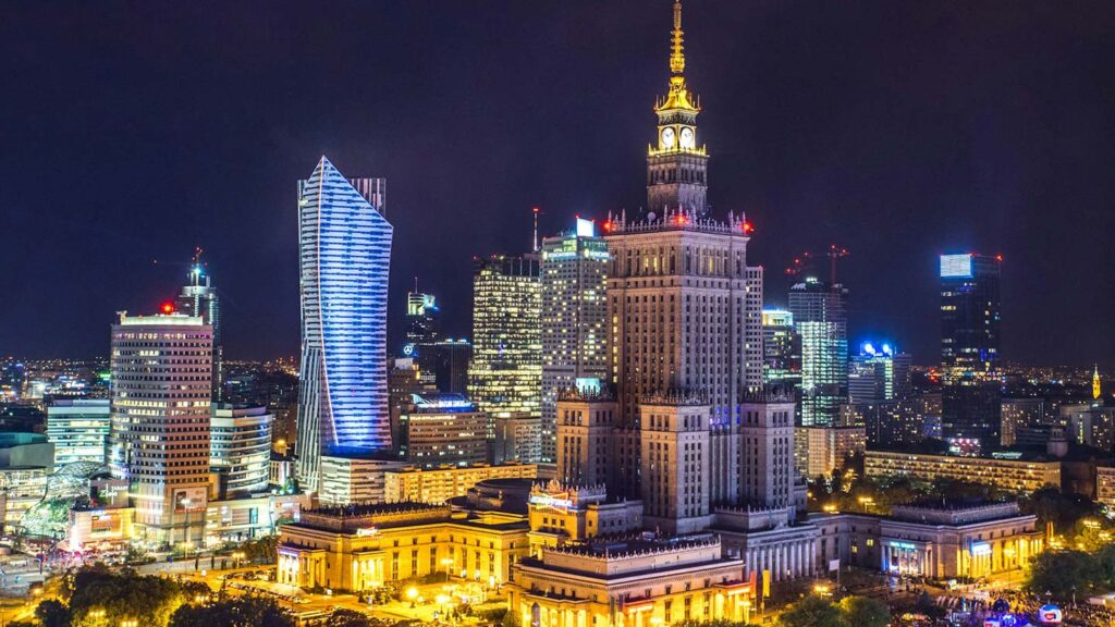 Kultur och vetenskapspalatset i Warszawa, omgiven av moderna skyskrapor, lysande nattscen.