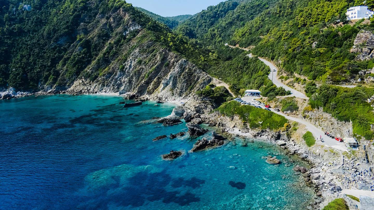Kustlinjen på ön Skopelos, med klart vatten och gröna berg.