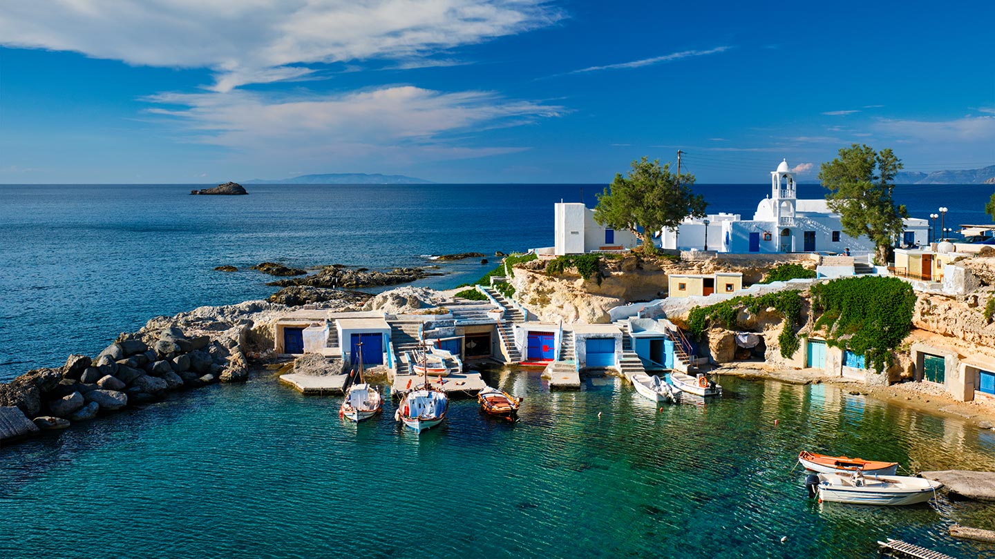 Mandraki på ön Milos, Grekland, med klara vatten och båtar vid stranden.