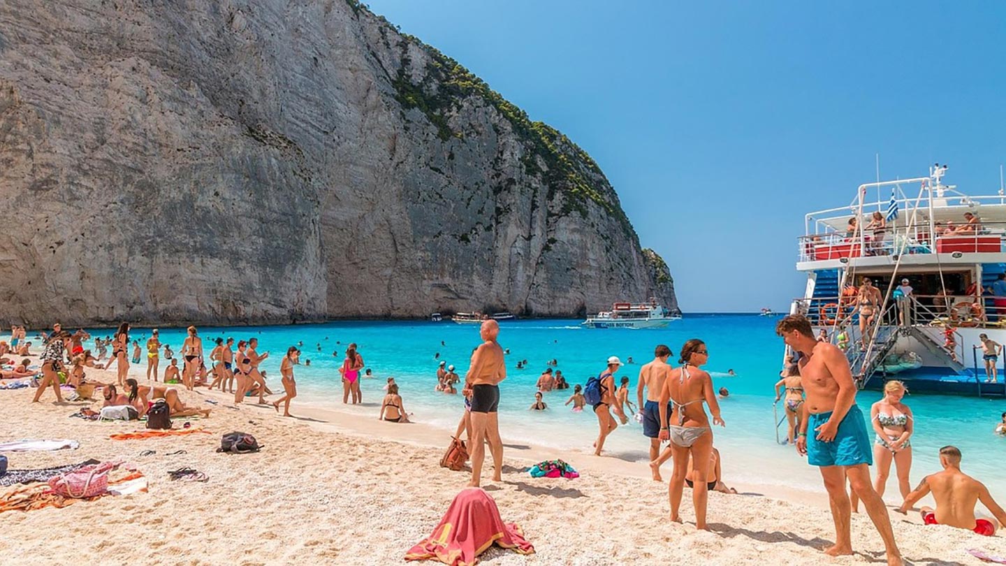 Navagio strand på Zakynthos, Grekland, med turister och klarblått vatten.