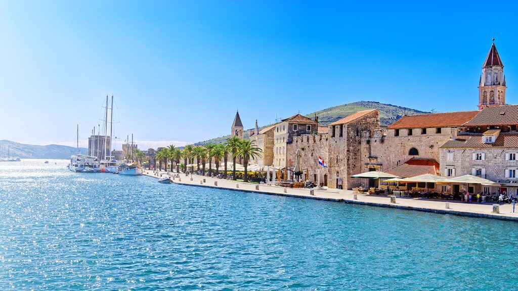 Panoramautsikt över Trogir, vackert kustområde med palmer och segelbåtar.