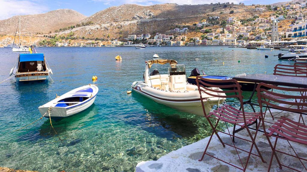 Bilden visar en panoramautsikt över den lilla oasen på ön Symi med båtar och vacker strand.