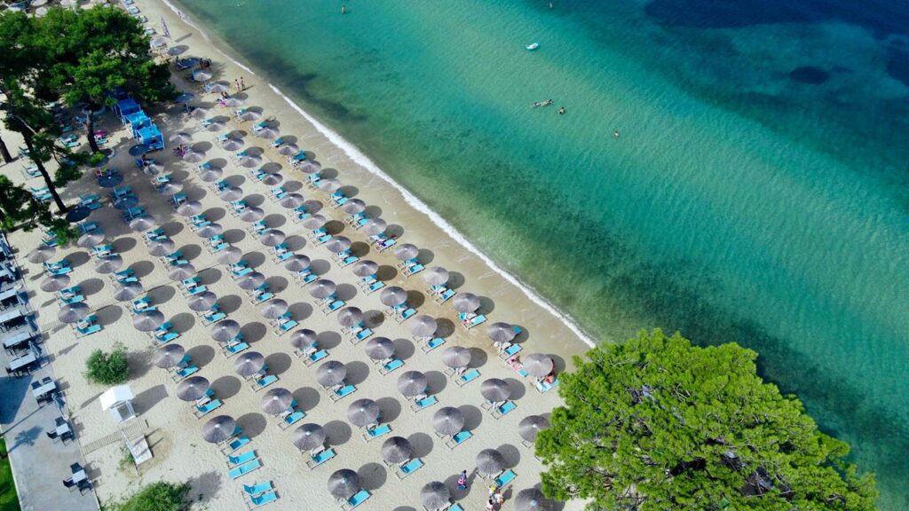 Rader av solstolar med parasoller på stranden i Thassos, Grekland. Turister njuter av solen.