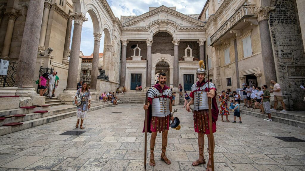 Romerska soldater poserar i Split, Kroatien, med turister i bakgrunden.