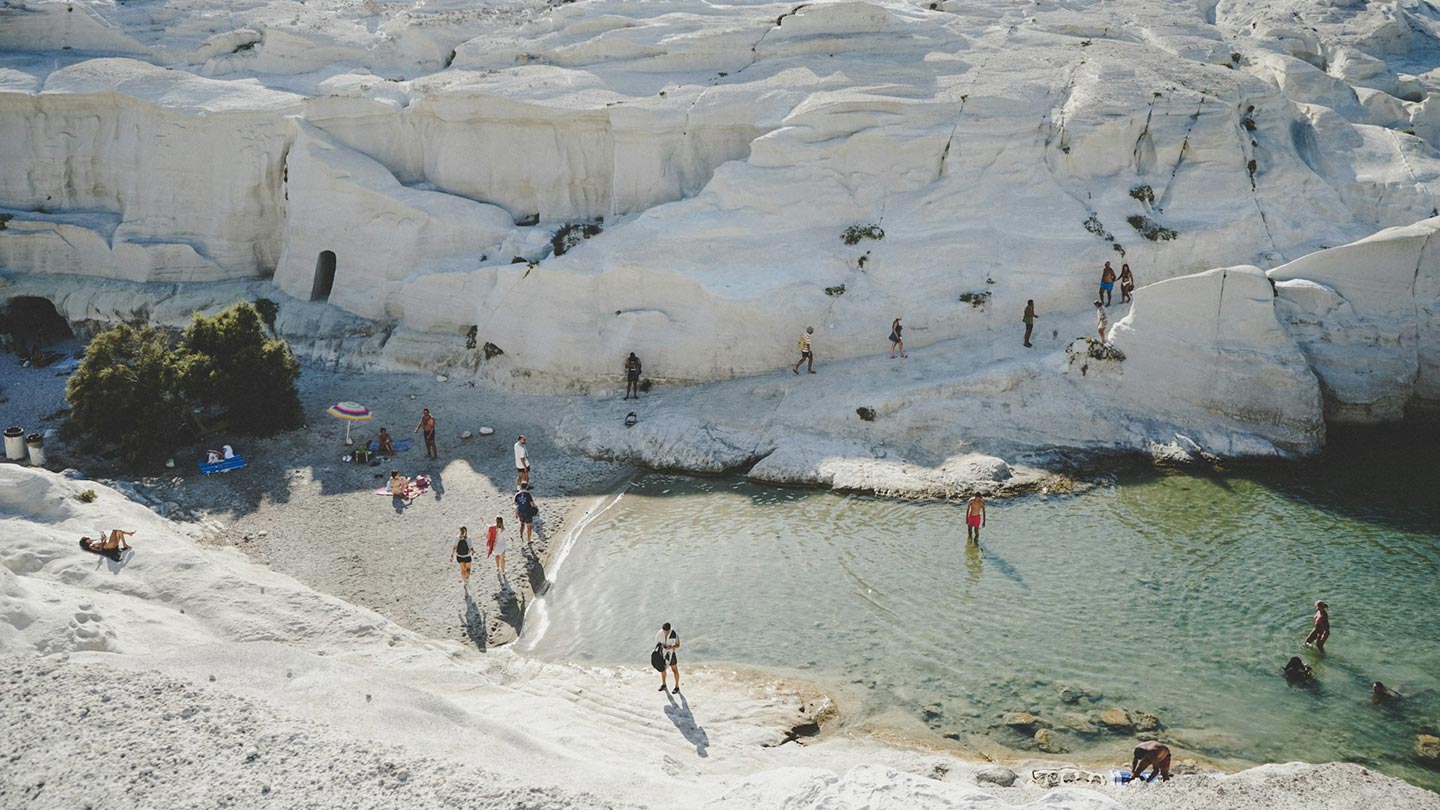Sarakiniko stranden på Milos, med vit klippformation och besökare som njuter av vattnet.