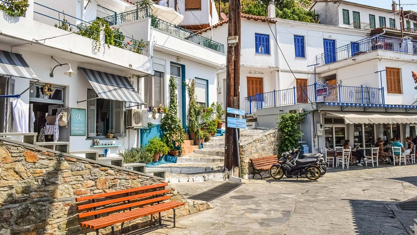 En solig gata i Skopelos, med butiker och uteserveringar.