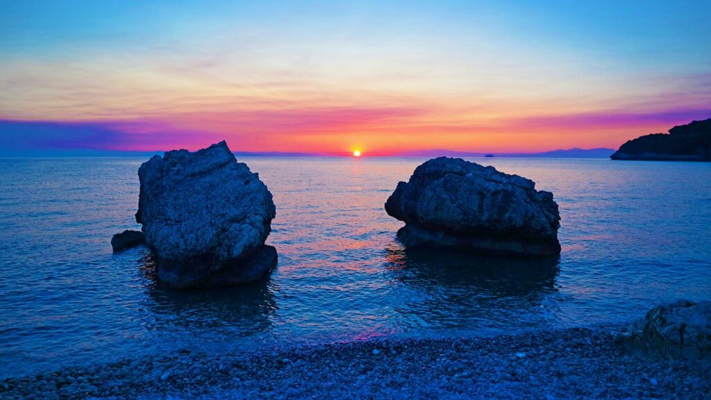 En vacker soluppgång över Kefalonia, med klippor och spegelblanka hav.