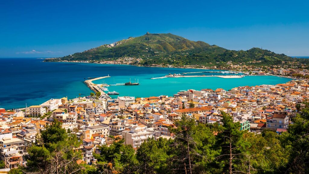En sommarutsikt över Zakynthos stad med vackert turkost hav och gröna berg.