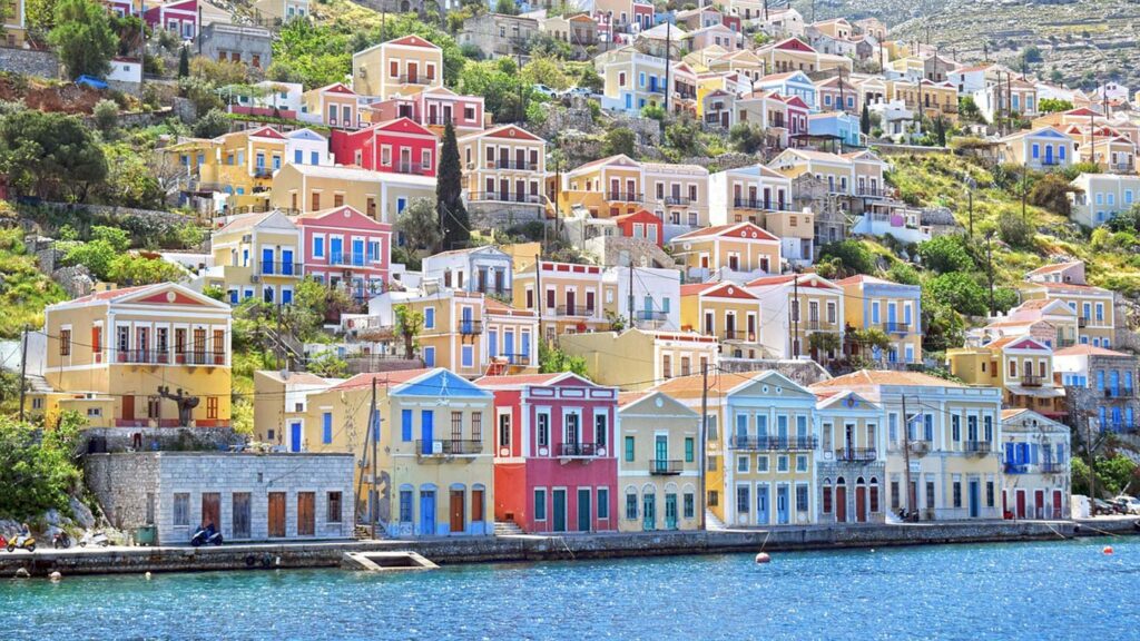Färgglada hus vid havet i Symi, Grekland, med vacker natur bakom.