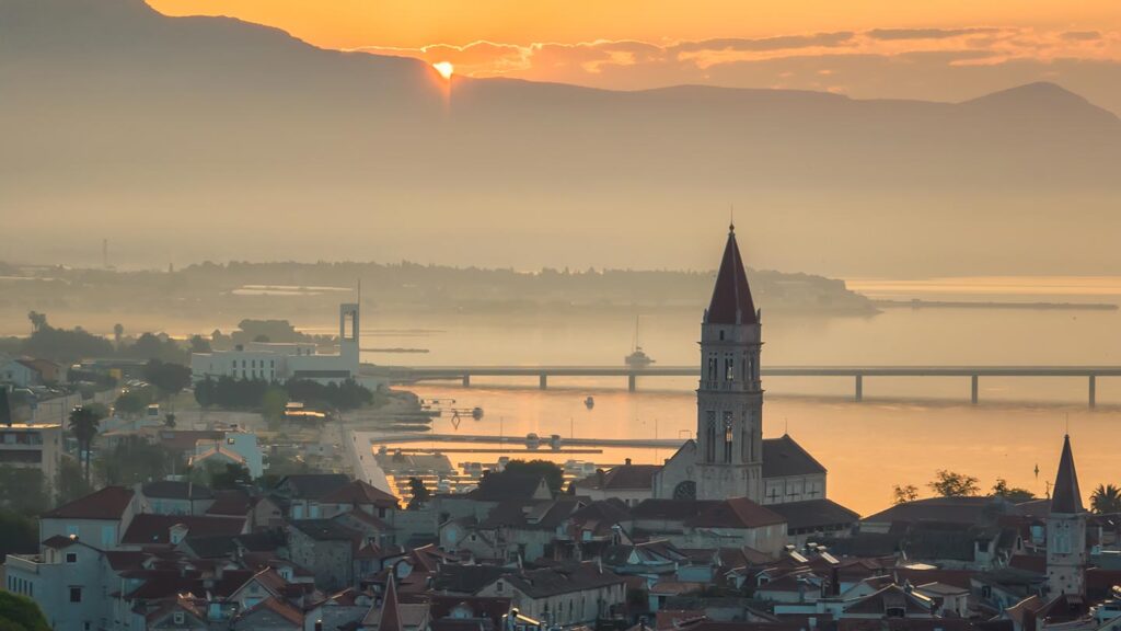 Trogir, Kroatien, med en vacker solnedgång bakom bergen och stilla vatten.