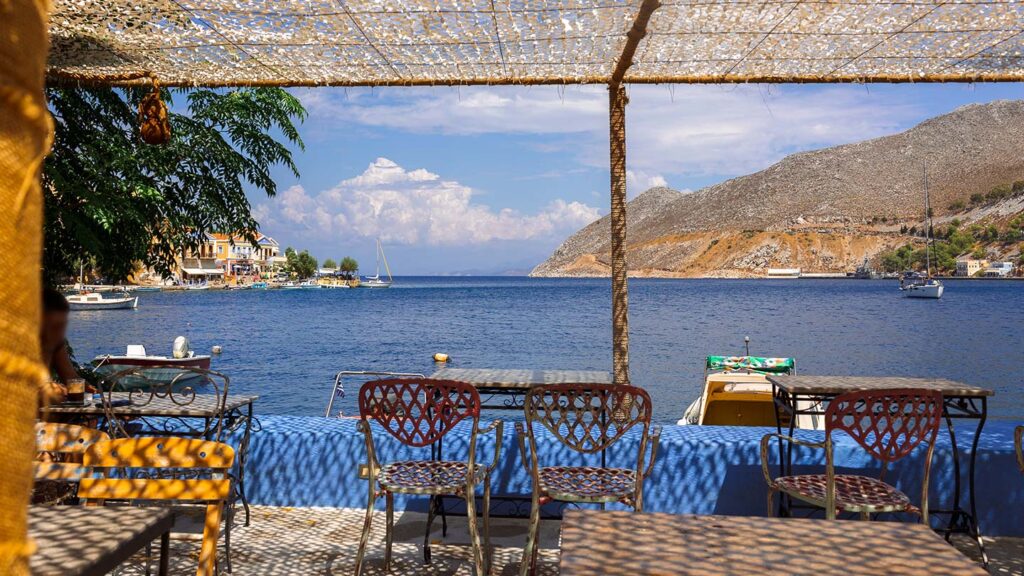 Uteservering på ön Symi, Grekland, med vacker havsutsikt och båtar.