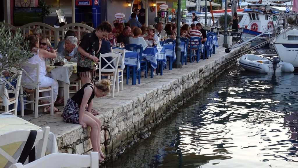 Uteservering vid piren i Fiscardo, Kefalonia, med gäster och båtar.