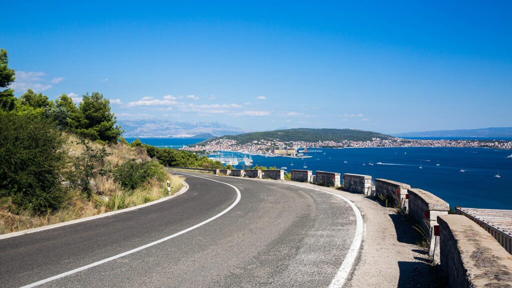 Utsikt över havsviken nära Trogir i Kroatien från en bergsväg, med klarblå himmel.