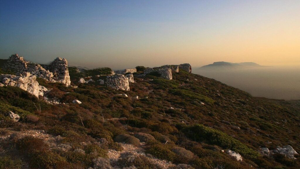 Vacker vy över ruiner i Kefalonia, med grönska och dimmiga bergen i bakgrunden.