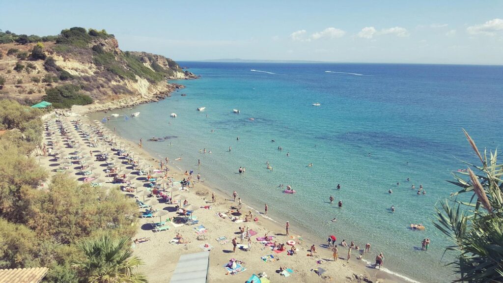 En vacker strand vid Xi Beach i Kefalonia, Grekland, med badande människor.