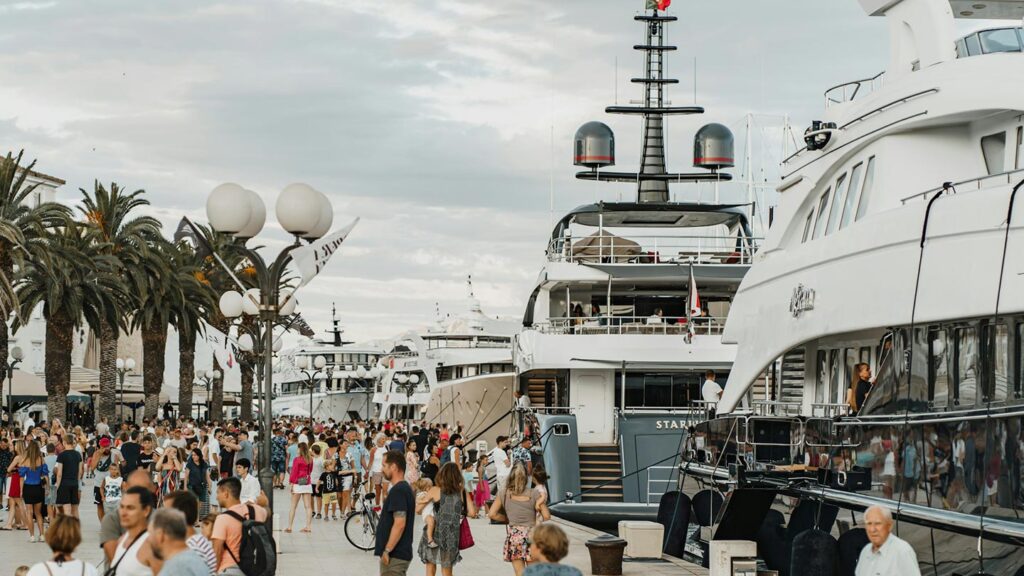 Många yachter i Trogir, Kroatien, med folkmassa och palmer i bakgrunden.